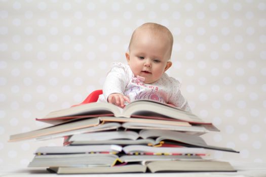 Cute baby girl sitting behind a pile of books