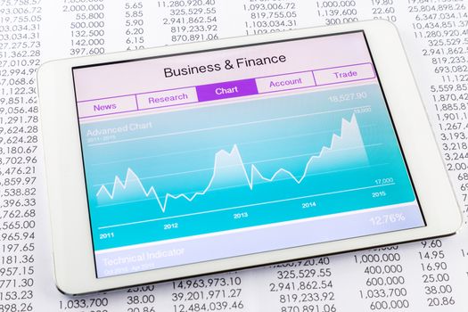 Advanced chart or graph with stock market data application on a digital tablet and papers with numbers on background