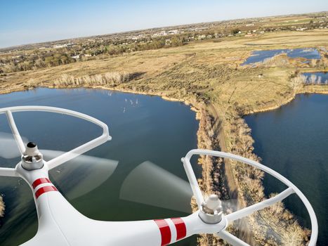 rotating propellers of an airborne quadcopter drone flying over lake and swamp landscape in northern Colorado, early spring