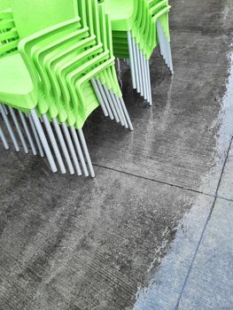 Stacks of green chairs on a sidewalk, on a rainy day.