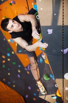 Young man practicing top rope climbing in indoor climbing gym, hands in focus