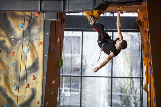 Young man practicing rock-climbing in indoor climbing gym