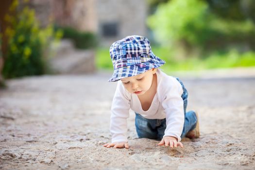 Cute little boy crawling on stone paved sidewalk