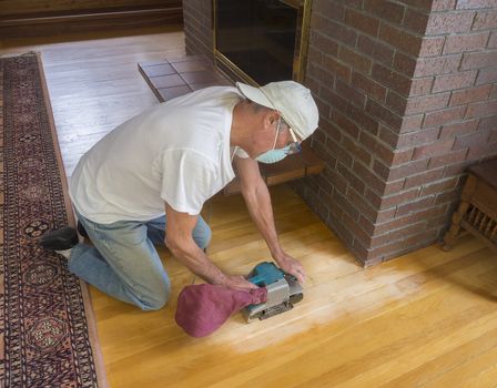 Older man using an electric sander on wood floor