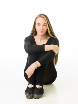 portrait of beautiful female gymnast sitting on white studio floor and smiling