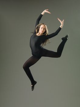 happy female dancer jumping against grey background