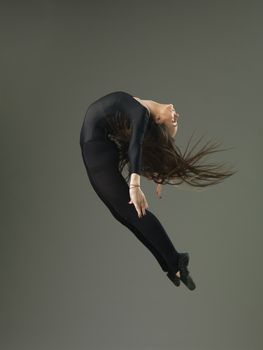 dancer performing high jump and backbend against grey background