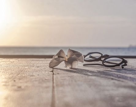 Glasses with clear lenses for vision correction and lotus flower lie on wooden table against blurred background seascape with sepia color correction