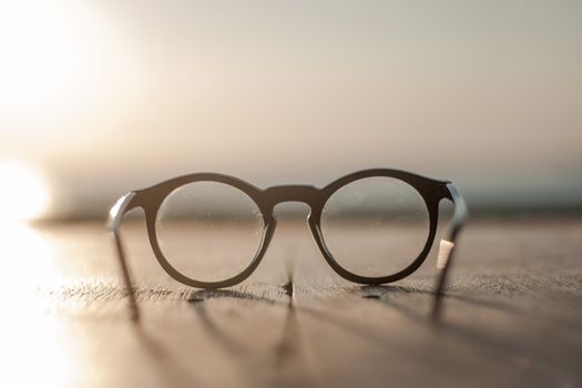 Glasses with clear lenses for vision correction lie on a wooden table against a blurred background seascape with sepia color correction and fronf view perspective