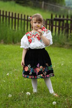 Little girl in traditional costume holding a dandelion in hand