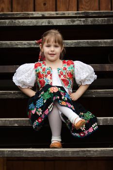 Small girl in traditional costume sitting on stairs