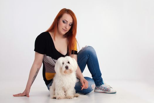 Young redhead woman with her white Maltese dog in studio