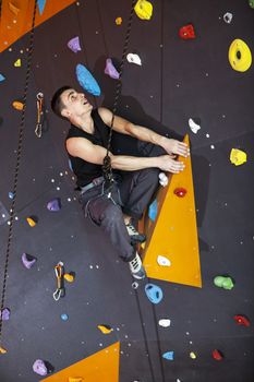 Young man practicing top rope climbing in indoor climbing gym