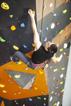 Young man practicing rock-climbing on a rock wall indoors