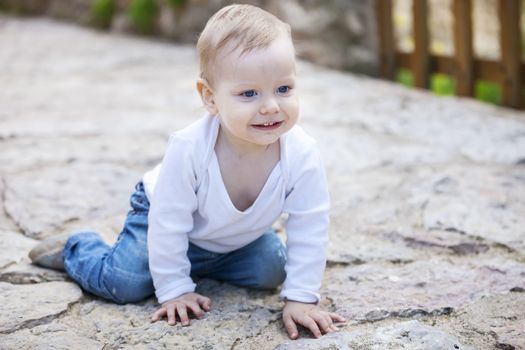 Cute little boy looking up and smiling while crawling on stone paved sidewalk