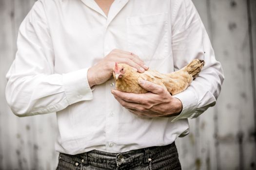 Farmer Holding a Beige Chicken in front of the Farm