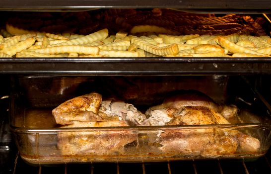Roasted pieces of fresh chicken and french fries on pan with shallow focus in oven