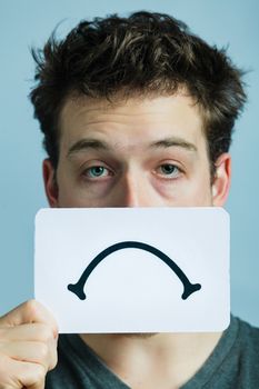 Unhappy Portrait of a Man Holding a Sad Mood Board with Blue Background