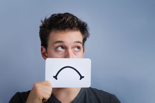 Unhappy Portrait of a Man Holding a Sad Mood Board with Blue Background