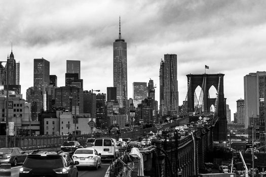 Traffic on Brooklyn bridge and New York City Manhattan downtown skyline at dusk with skyscrapers over East River panorama. Black and white.