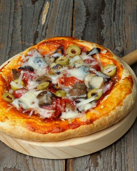 Homemade Pizza Green Olives, Salami, Mushrooms and Grated Cheese on Circle Cutting Board closeup on Wooden background