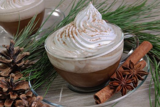 Cup of coffee with whipped cream and cinnamon on the table with pine cones