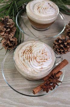 Cup of coffee with whipped cream and cinnamon on the table with pine cones