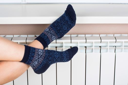 Woman's legs in socks on white radiator background