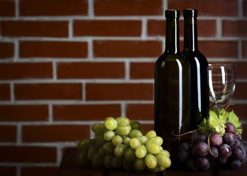 Wite and red wine bottles with grape on brick wall background