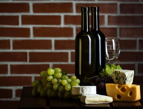 Wine bottles with grape and cheese on brick wall background