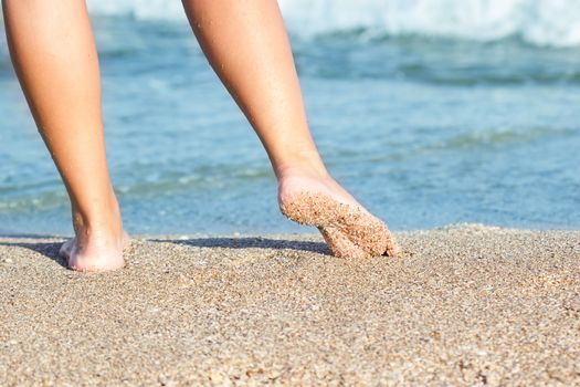 Closeup view of female feet and golden sand on beach with blue sea background