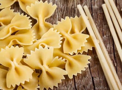 Raw bow tie pasta and spaghetti on wooden background