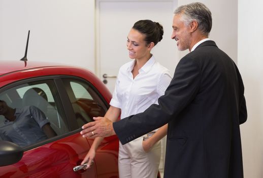 Businessman showing a car to a woman at new car showroom
