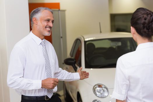 Businessman showing a car to a woman at new car showroom