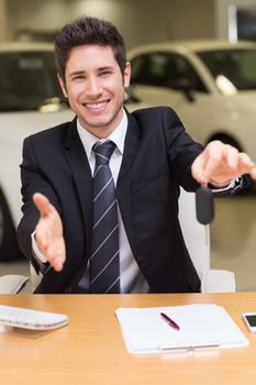 Man giving a customer keys while reaching for handshake at new car showroom