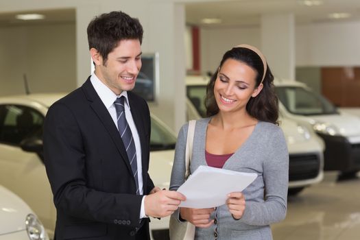 Salesperson showing clipboard to sign to customer at new car showroom