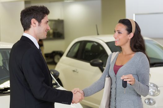 Businessman giving car key while shaking a customer hand at new car showroom