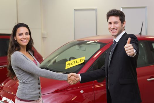 Person shaking hands in front of a sold car at new car showroom
