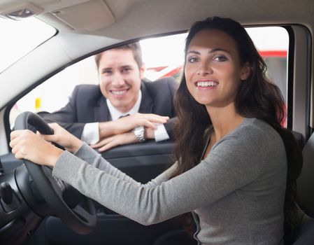 Happy female driver at the wheel sitting in her car at new car showroom