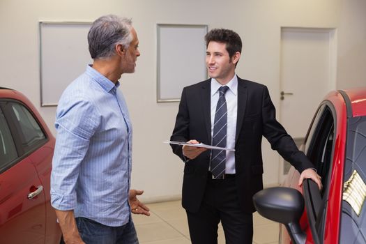 Smiling businessman speaking with his customer at new car showroom