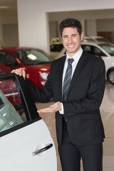 Smiling businessman showing a car for sale at new car showroom
