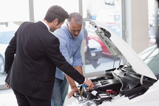 Two men looking at a car engine at new car showroom