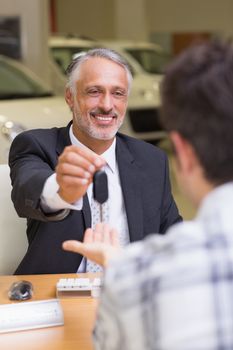 Smiling salesman giving a customer car keys at new car showroom