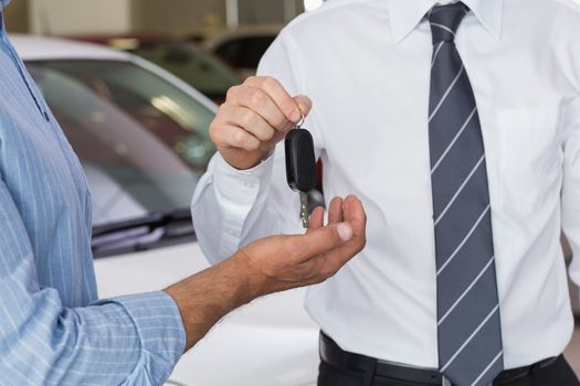 Businessman giving car key to customer at new car showroom