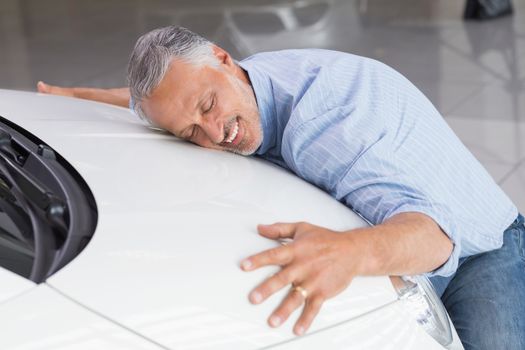 Smiling man hugging a white car at new car showroom