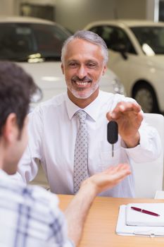 Smiling salesman giving a customer car keys at new car showroom