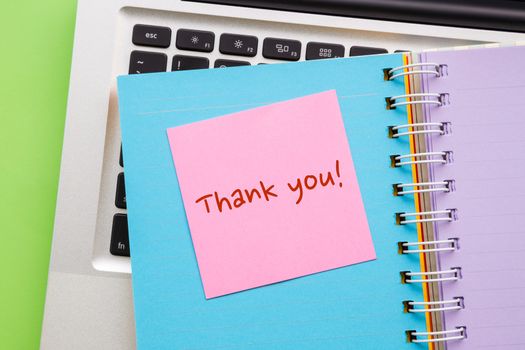Close up pink notepad with word " Thank You " putting on colorful paper book with laptop