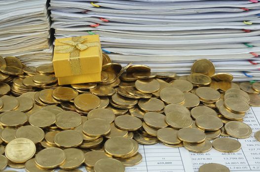 Gift box in heap of gold coins with pile of paperwork.                               