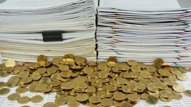 Many gold coins was put together in front of a pile of old documents.                               