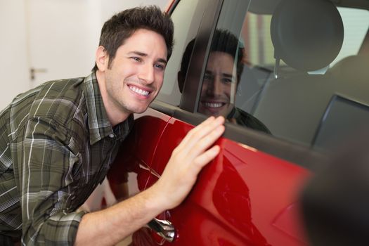 Smiling man hugging a red car at new car showroom